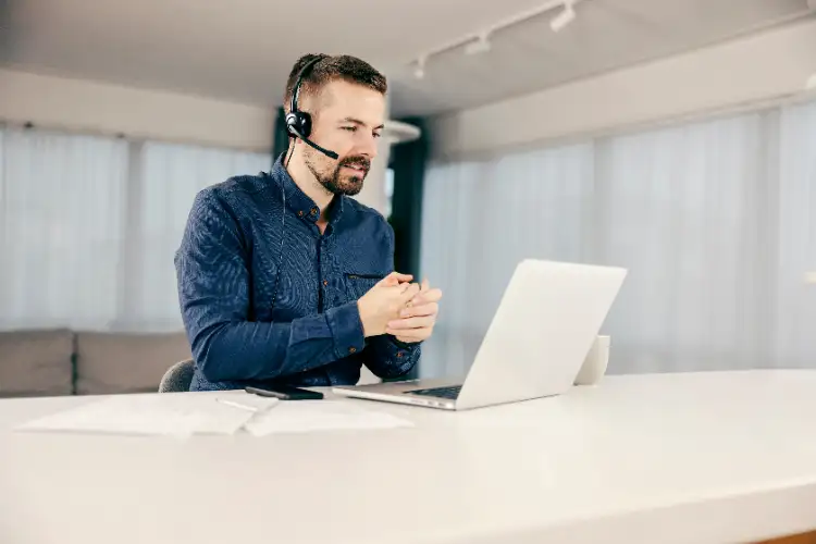 Ein Herr mit dunkelblauem Hemd hat ein schwarzes Headset auf und gibt über sein Notebook Support.